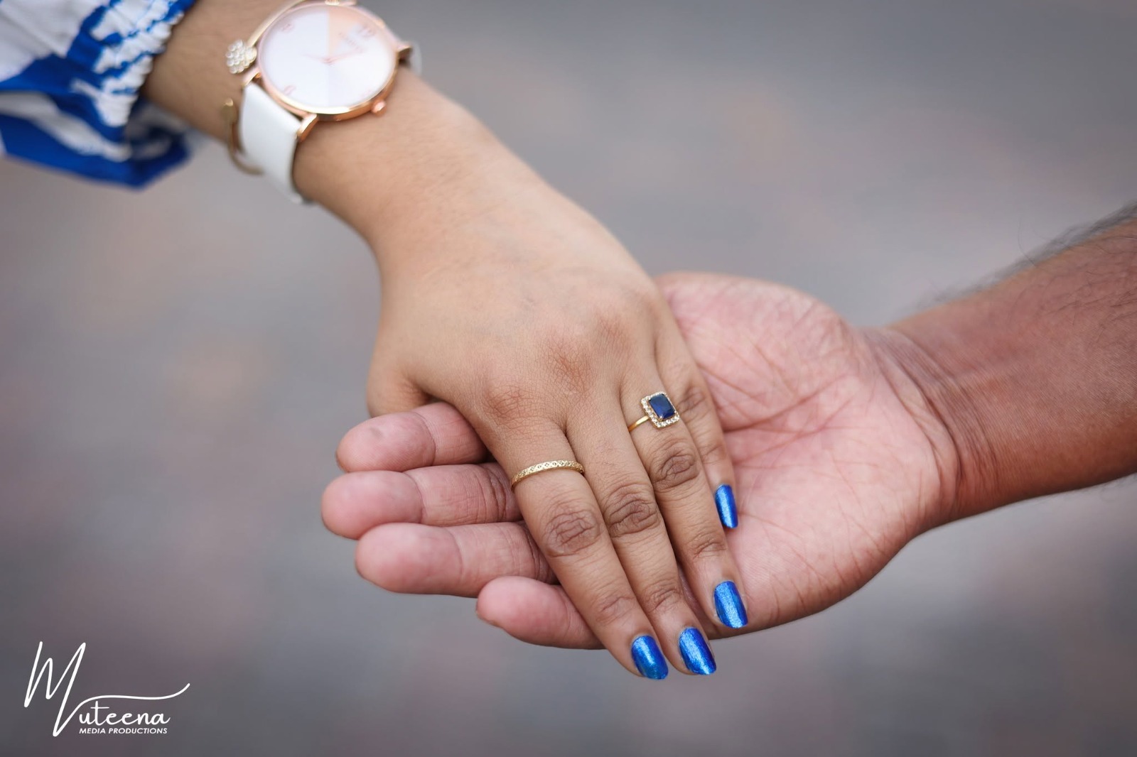 Couple's hands photographed close-up — a woman's hand with a sapphire engagement ring and blue nail polish resting in a man's palm — engagement detail Dubai