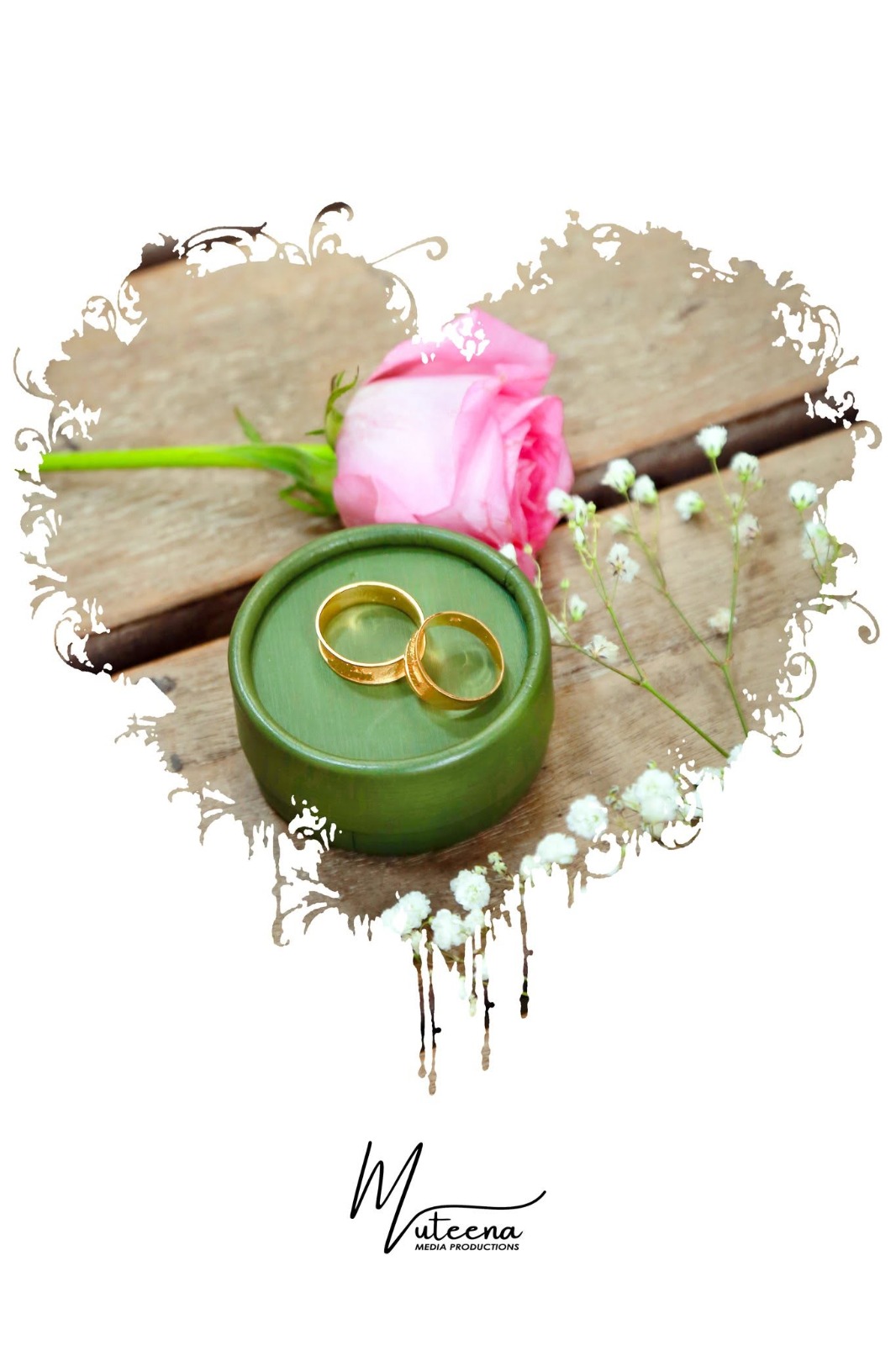 Pair of gold wedding rings resting in a green wooden box beside a pink rose and baby's breath on rustic timber, inside a hand-drawn heart border — wedding detail photography Dubai