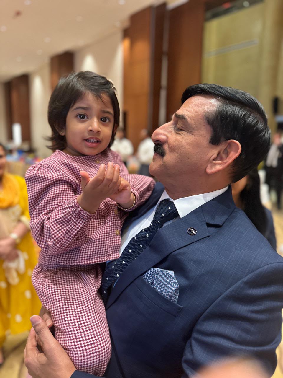 Grandfather in navy suit holding a young child at a family gathering in Dubai