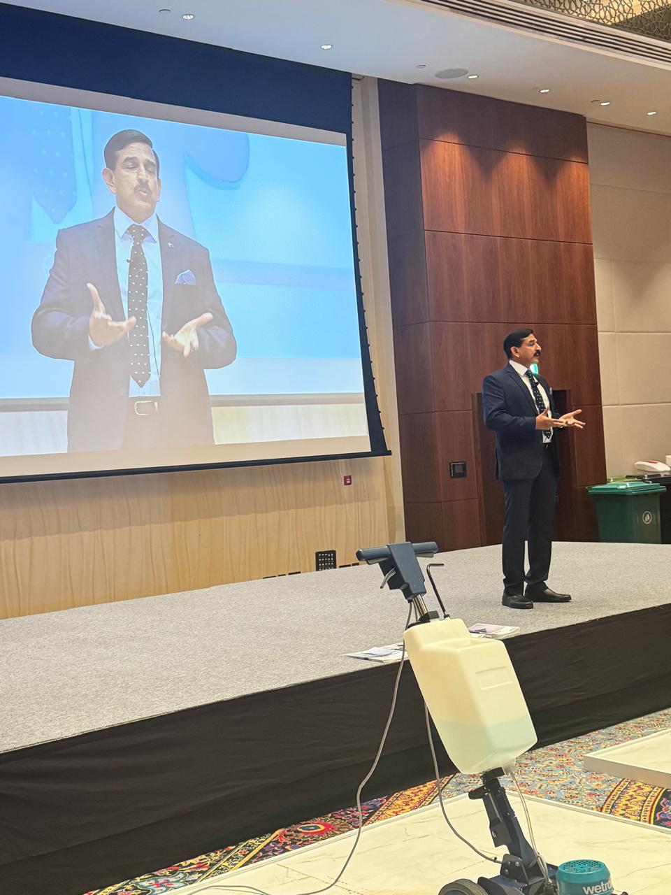 Keynote speaker on stage at a corporate conference in Dubai with projection screen
