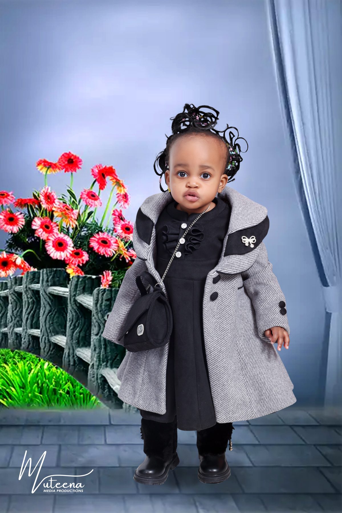 Toddler girl in a grey coat with a handbag photographed on a painted garden backdrop at Dar Al Muteena Studio